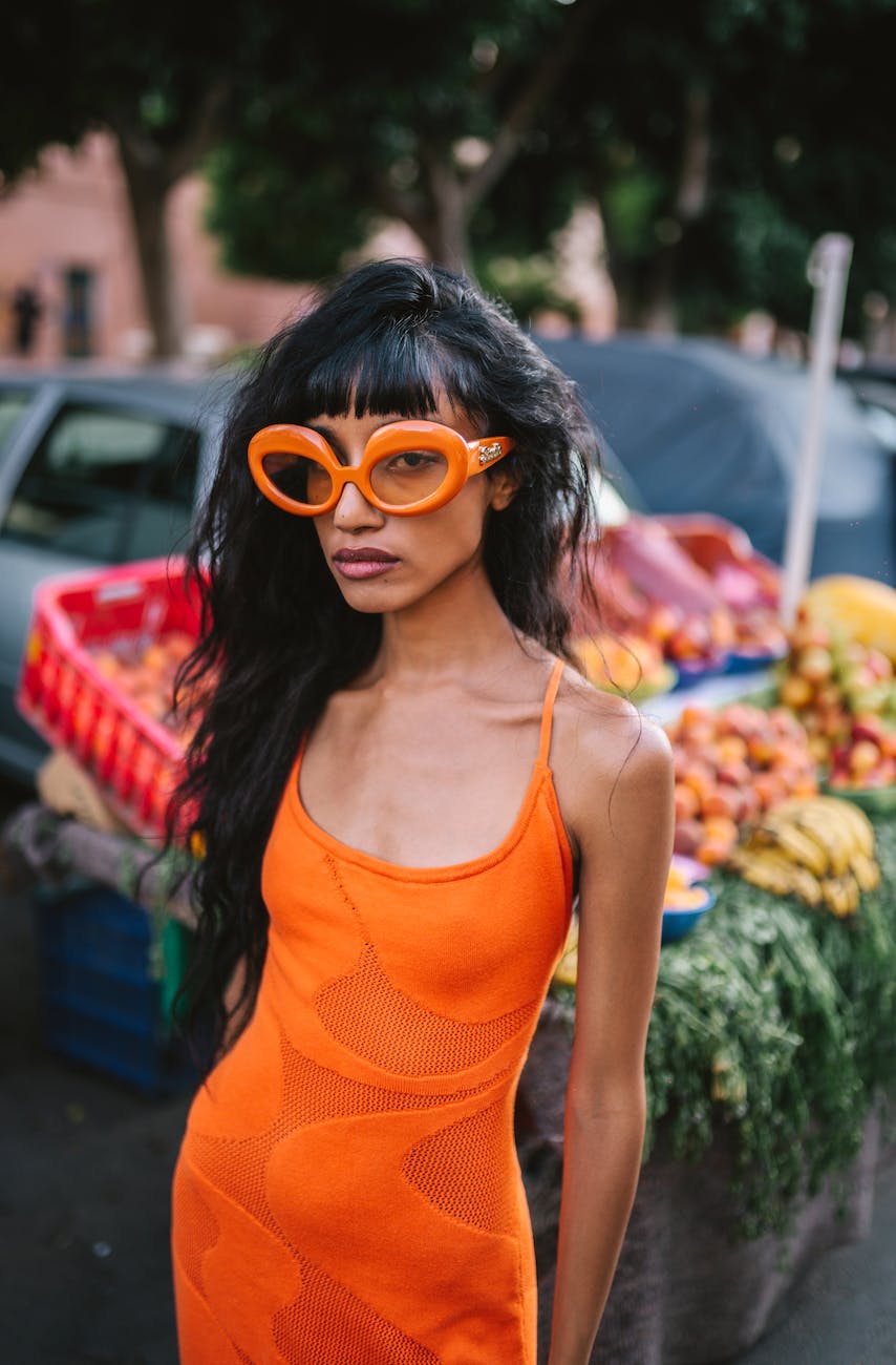 young woman in an orange dress and glass standing on the street